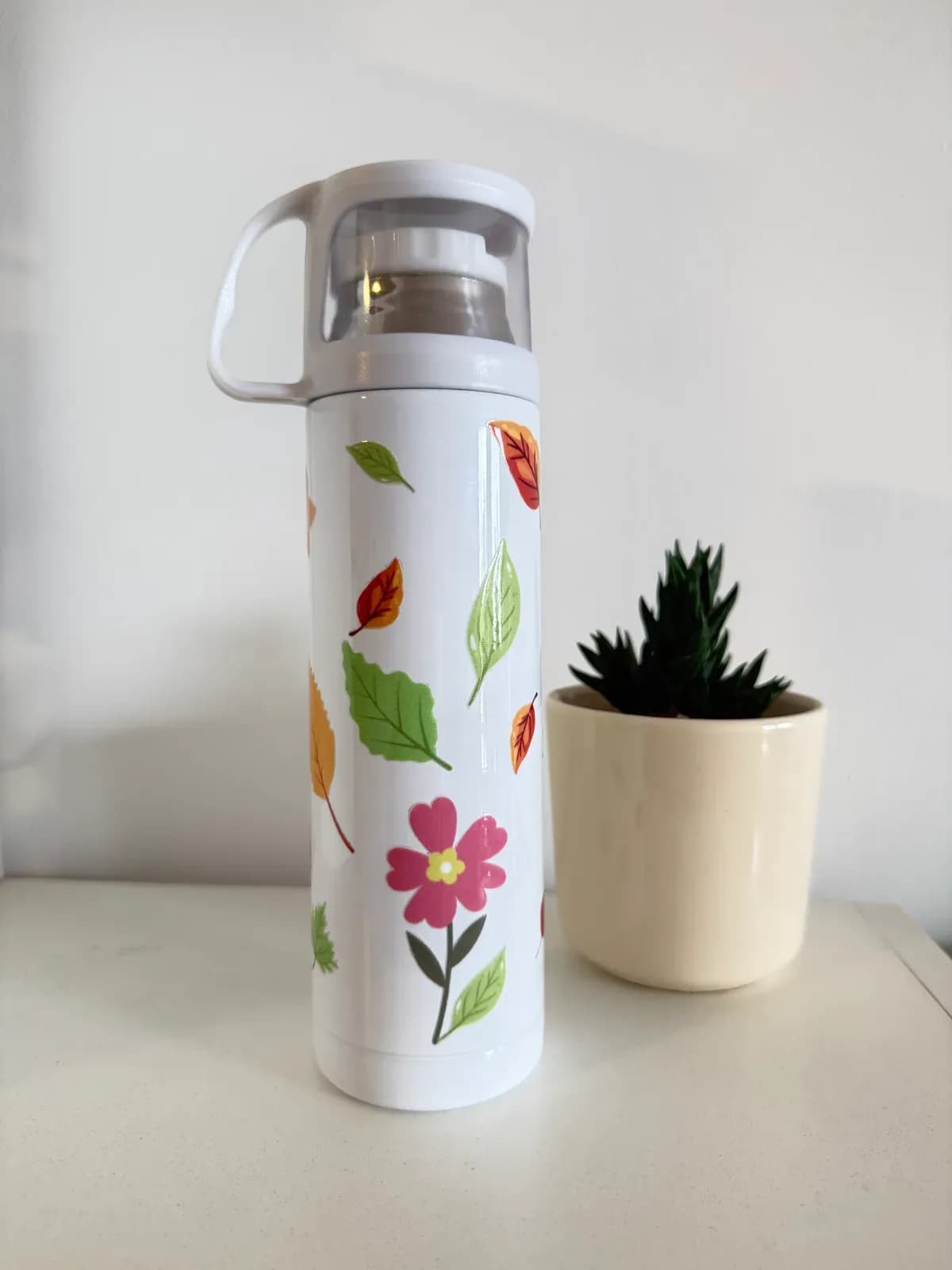 Termo blanco con tapa-taza y estampa de hojas y flores