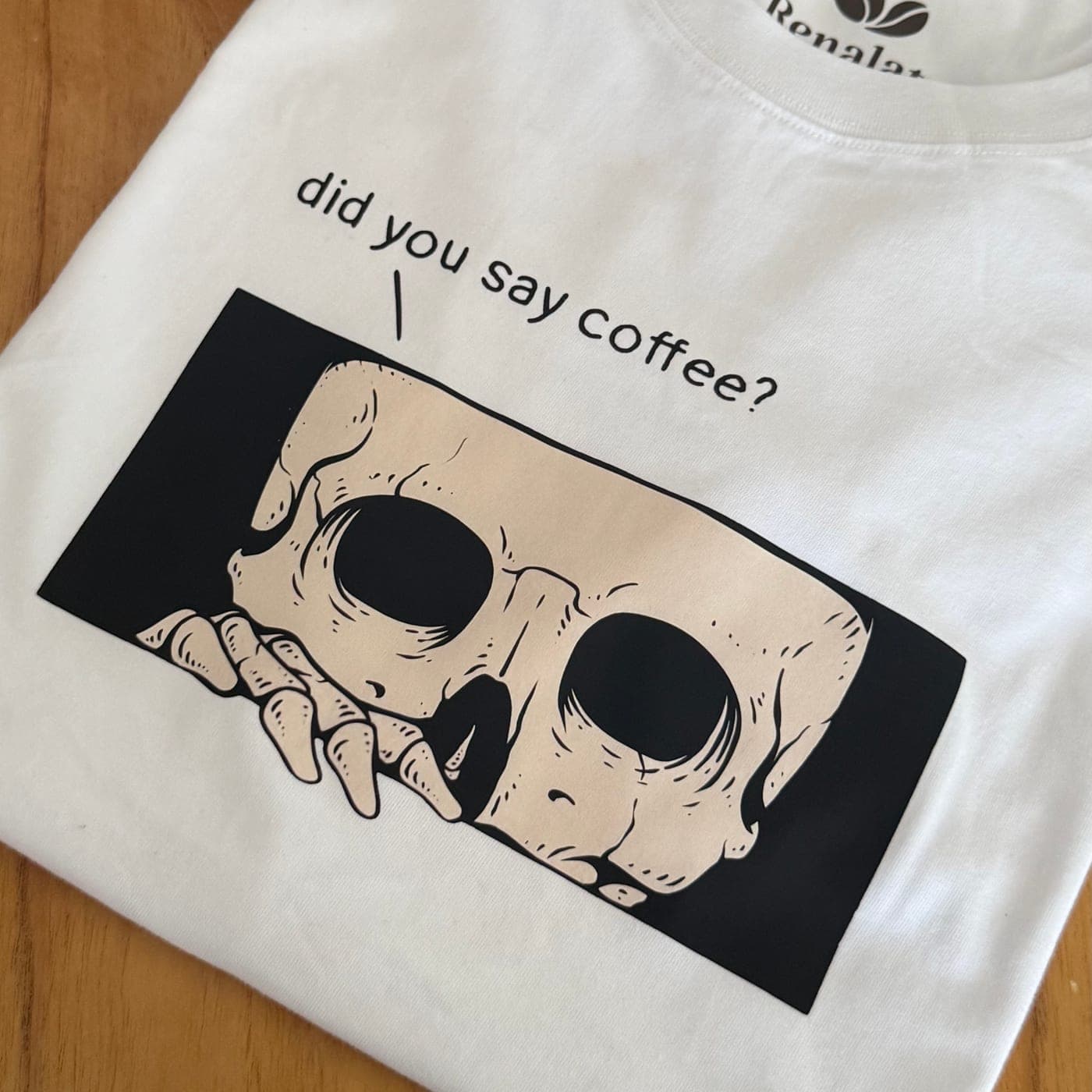 Una calavera que se asoma apenas escucha la palabra mágica. Para quienes no funcionan hasta la primera taza. Color blanco, estampa en negro y beige.